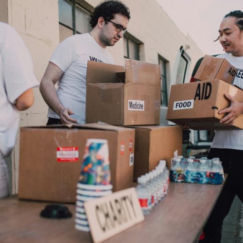 Volunteers loading aid boxes with food and medicine from a van outdoors.